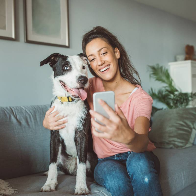 A woman takes a selfie with a black-and-white dog on a couch